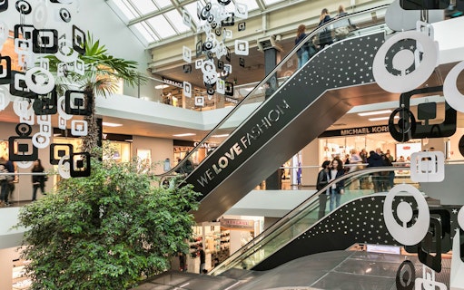 Escalator at FoxTown Designer Outlet with shoppers and store signs, including Michael Kors.