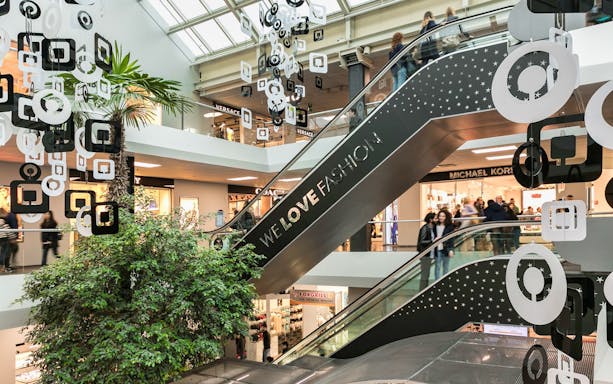 Escalator at FoxTown Designer Outlet with shoppers and store signs, including Michael Kors.
