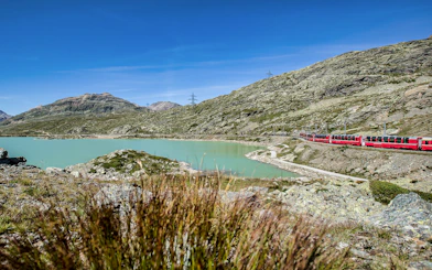 Bernina Express train passing by a turquoise lake in the Swiss Alps on the way to St. Moritz.