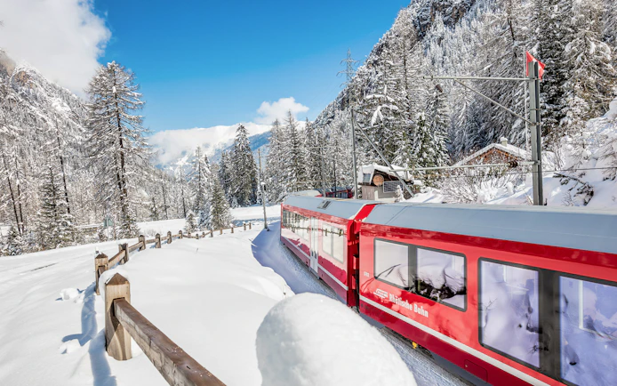 Bernina Express train traveling through snowy Alps on a full-day tour from Milan to St. Moritz.