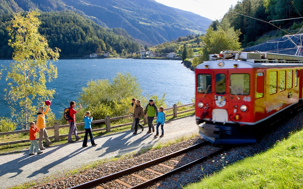 Bernina Express train passing by hikers near a lake in the Swiss Alps, close to St. Moritz.