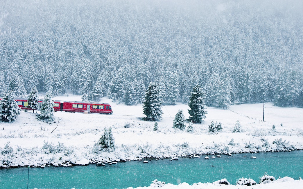 Red Bernina Express train traveling through snowy landscape near St. Moritz.