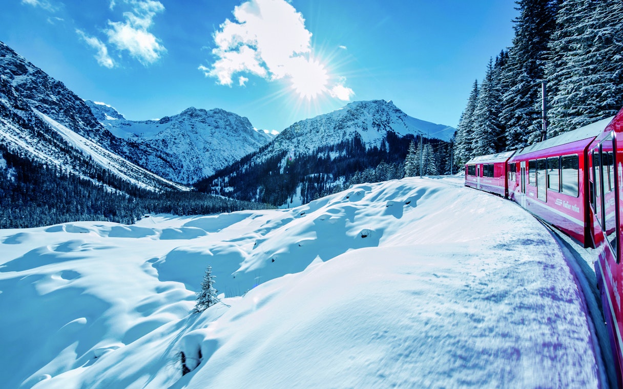 Red Bernina Express train traveling through snowy Alps on a full-day tour from Milan to St. Moritz.