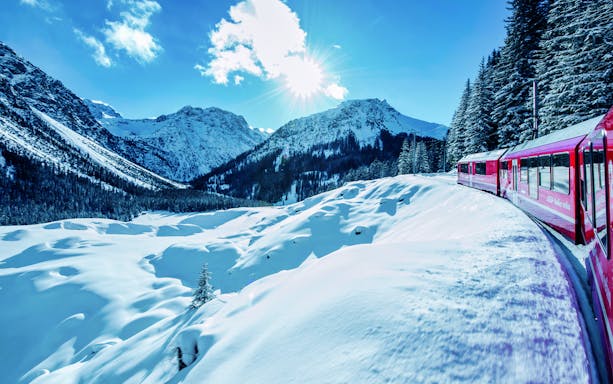 Red Bernina Express train traveling through snowy Alps on a full-day tour from Milan to St. Moritz.
