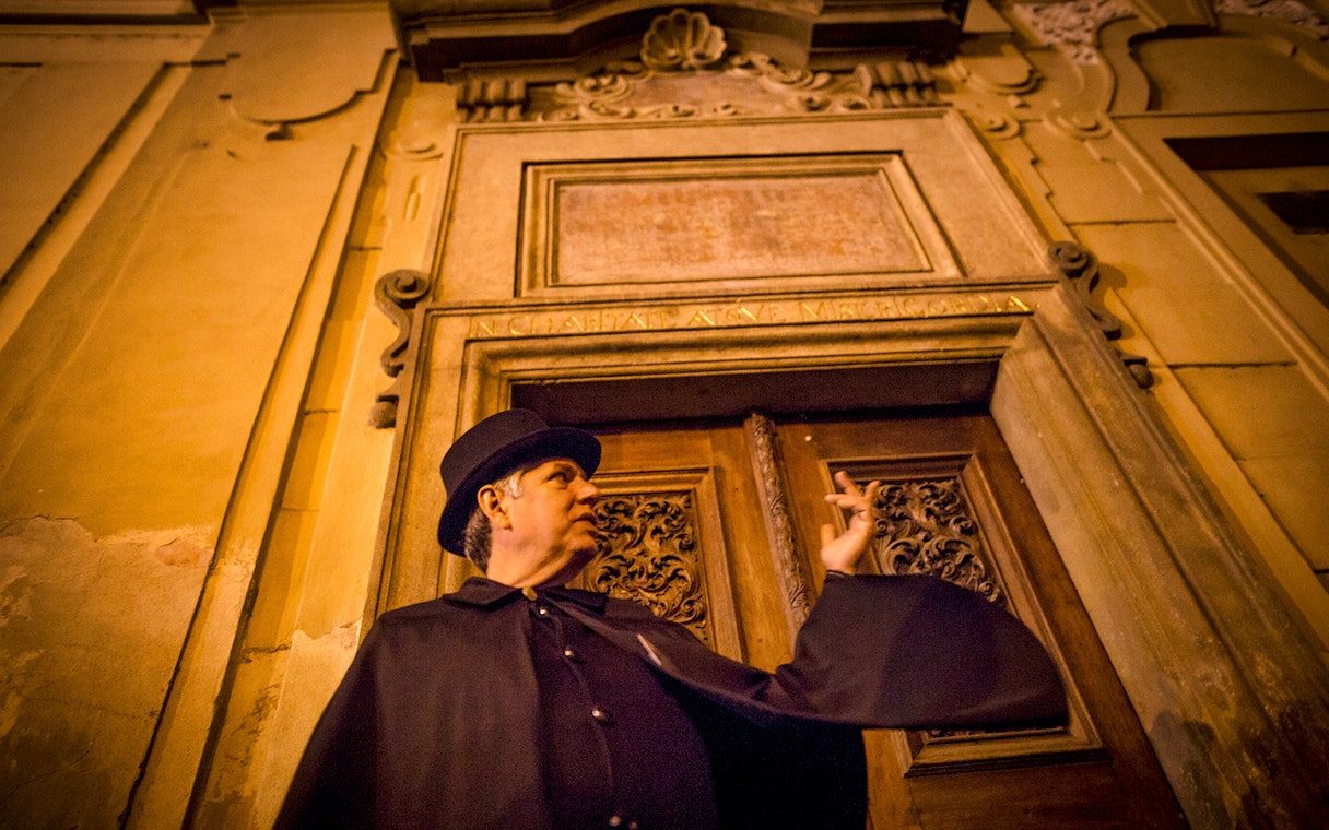 Guide in cloak gestures during Prague Old Town ghost tour.