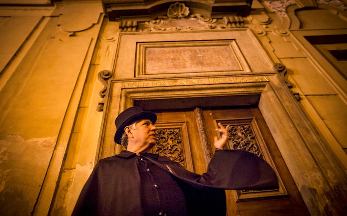 Guide in cloak gestures during Prague Old Town ghost tour.