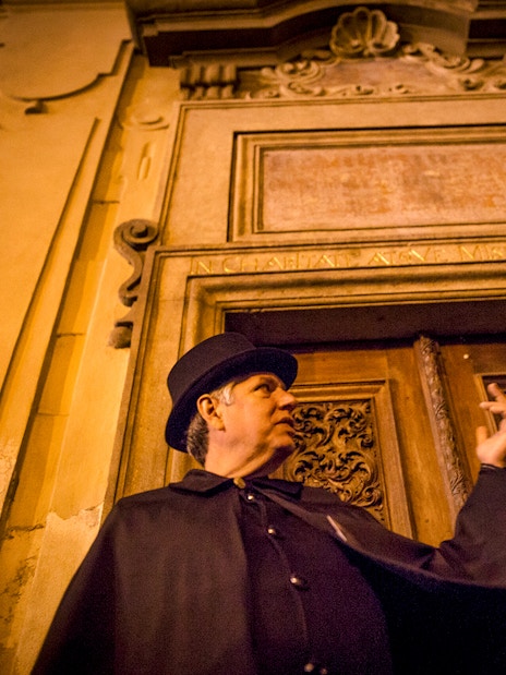 Guide in cloak gestures during Prague Old Town ghost tour.