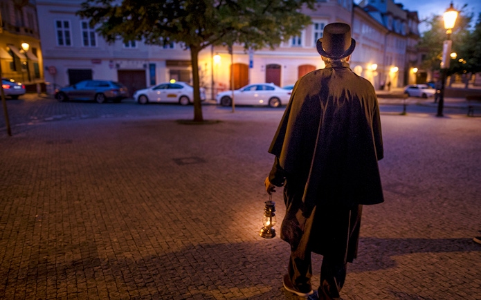 Guide in cloak and top hat holding lantern on Prague evening ghost tour.