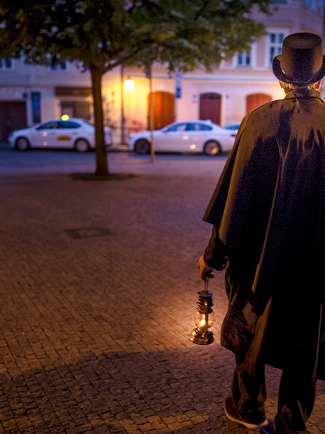 Guide in cloak and top hat holding lantern on Prague evening ghost tour.