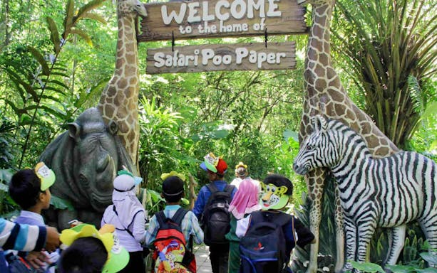 Children entering Bali Safari and Marine Park under a sign with animal sculptures.