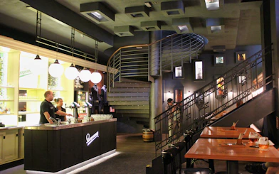 Prague brewery interior with bar counter, staff, and spiral staircase.