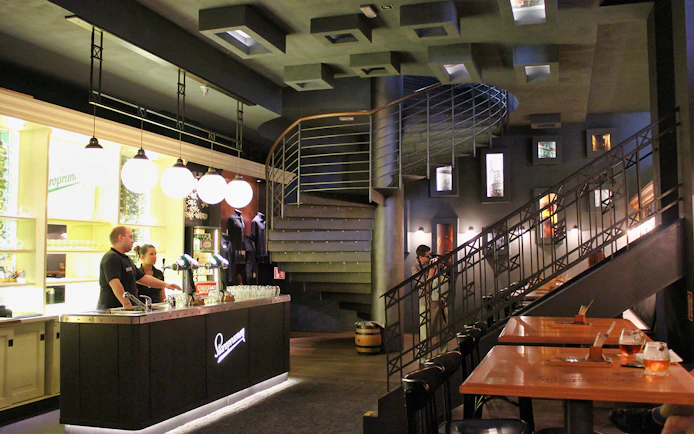 Prague brewery interior with bar counter, staff, and spiral staircase.
