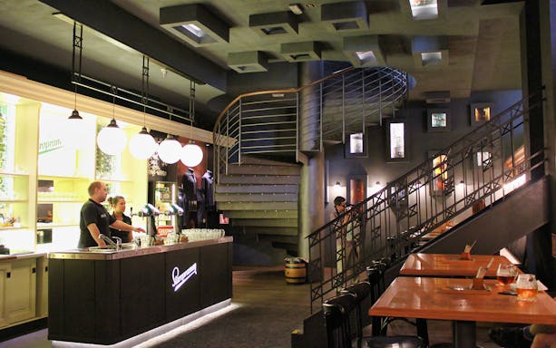 Prague brewery interior with bar counter, staff, and spiral staircase.