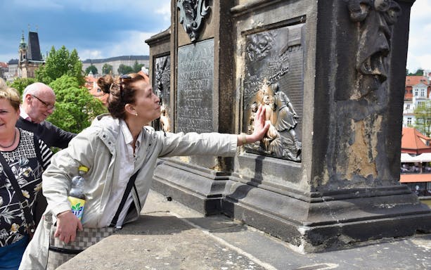 Tourists touching relief on Charles Bridge during Prague walking tour.
