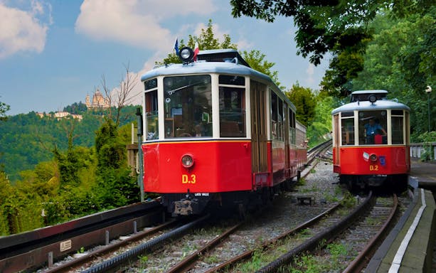Red trams on tracks with hilltop basilica view, Turin sightseeing tour.
