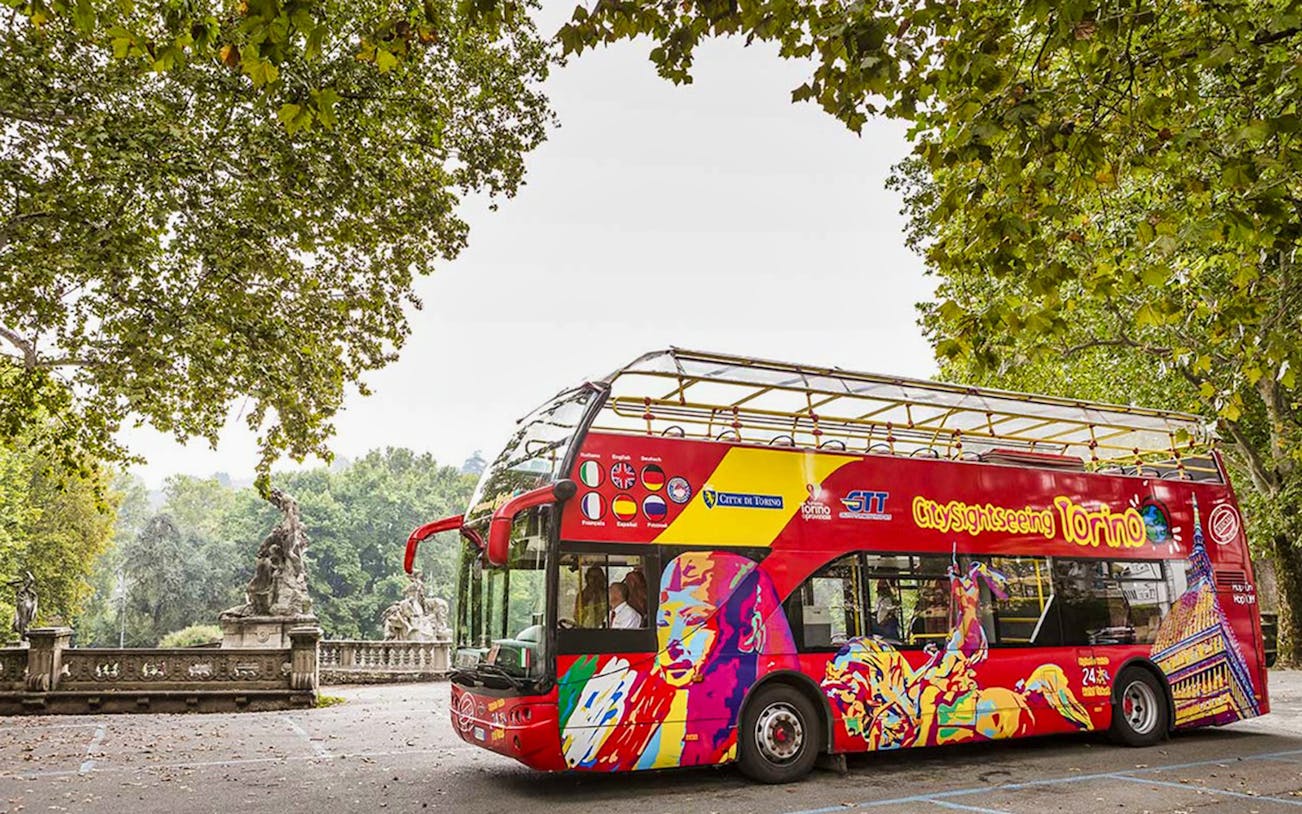 Tour bus for City Sightseeing Turin 48Hr Hop-On-Hop-Off Tour parked near trees.