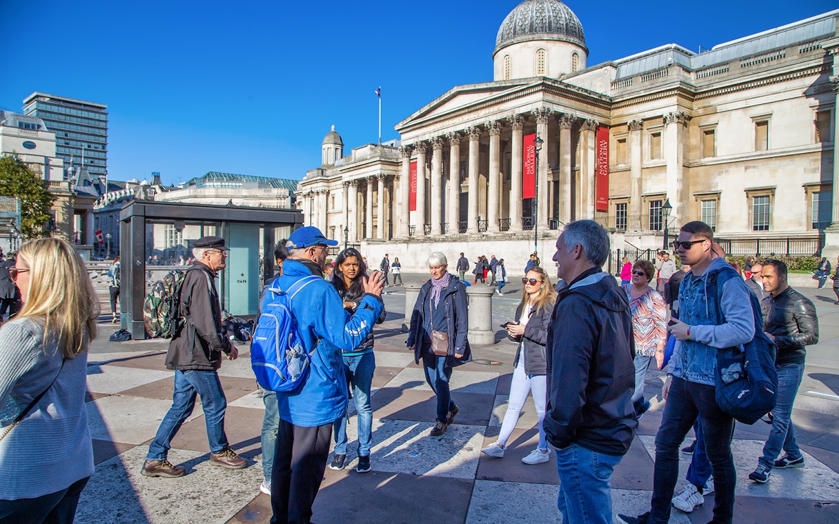 Tour group in Trafalgar Square, London, with guide explaining landmarks.