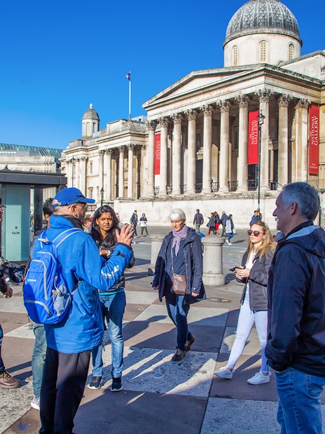 Tour group in Trafalgar Square, London, with guide explaining landmarks.