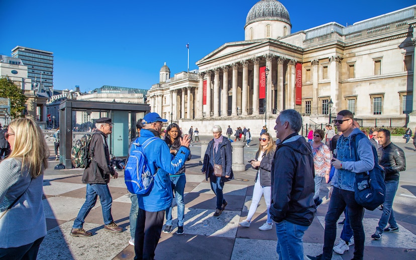 Tour group in Trafalgar Square, London, with guide explaining landmarks.