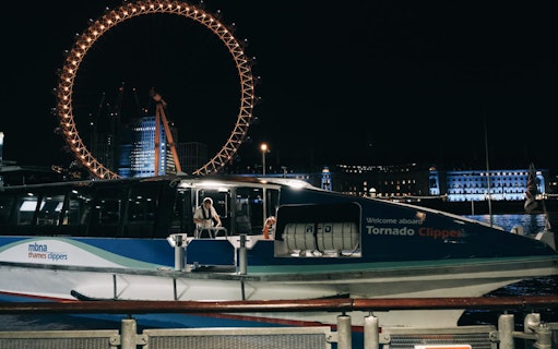 Boat docked at night with illuminated Ferris wheel in London, part of Magic of Film Experience.