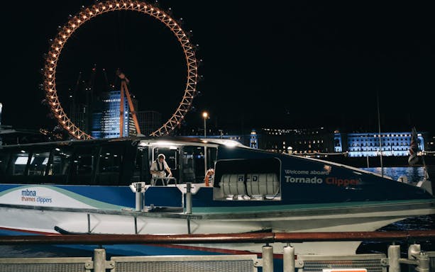 Boat docked at night with illuminated Ferris wheel in London, part of Magic of Film Experience.