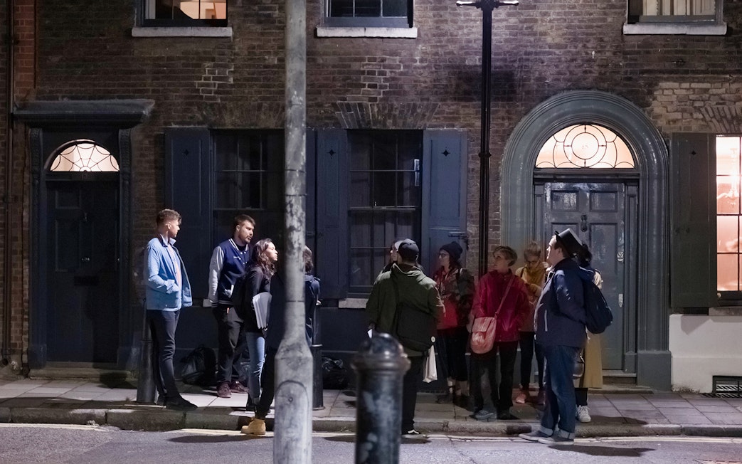 Group of people on a Jack the Ripper tour standing outside historic London building at night.
