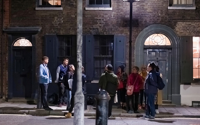 Group of people on a Jack the Ripper tour standing outside historic London building at night.
