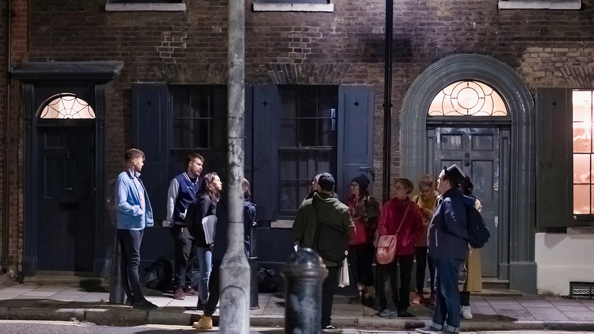 Group of people on a Jack the Ripper tour standing outside historic London building at night.