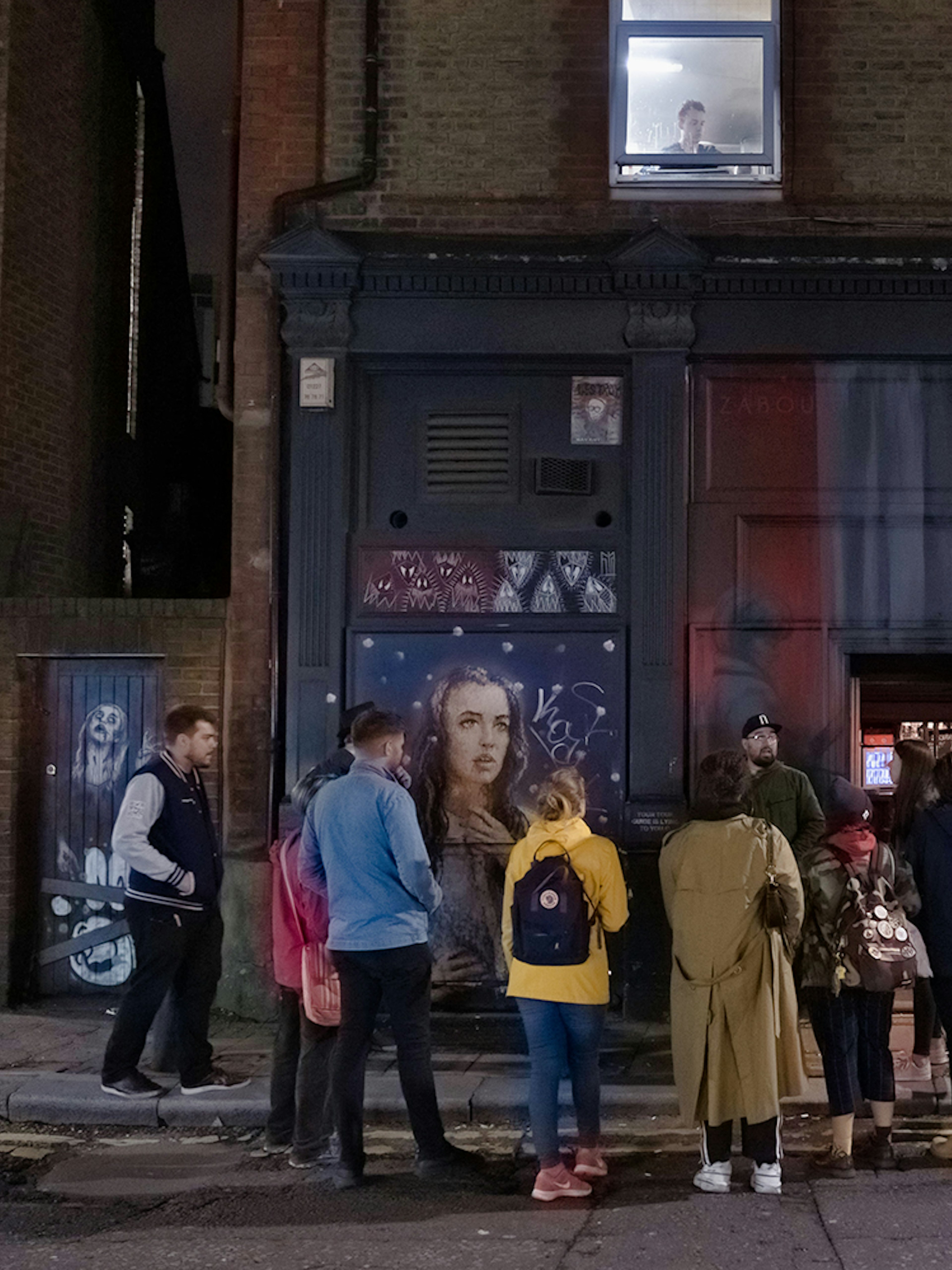 Group of people on a Jack the Ripper tour outside a mural-covered building in London.