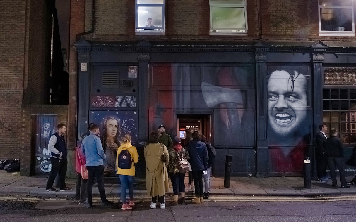 Group of people on a Jack the Ripper tour outside a mural-covered building in London.