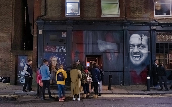 Group of people on a Jack the Ripper tour outside a mural-covered building in London.