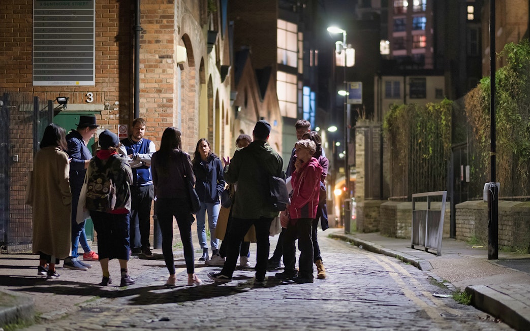 Group of people on a nighttime Jack the Ripper tour in a historic London alley.