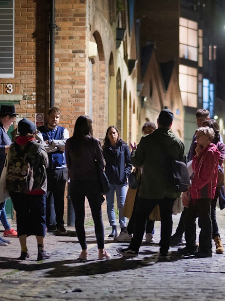 Group of people on a nighttime Jack the Ripper tour in a historic London alley.