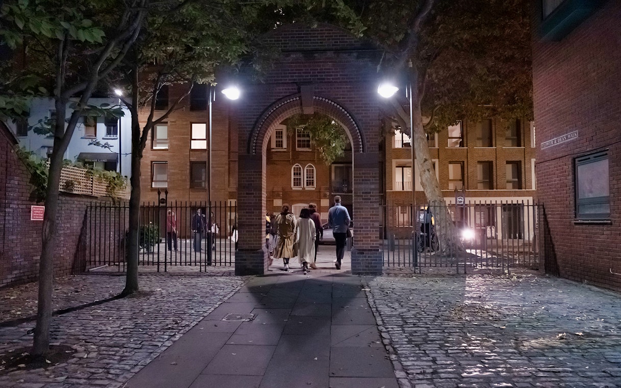Group walking through a brick archway on a Jack the Ripper tour in London at night.