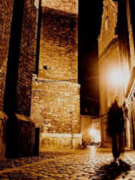 Shadowy figure walking down a dimly lit cobblestone alley in London.