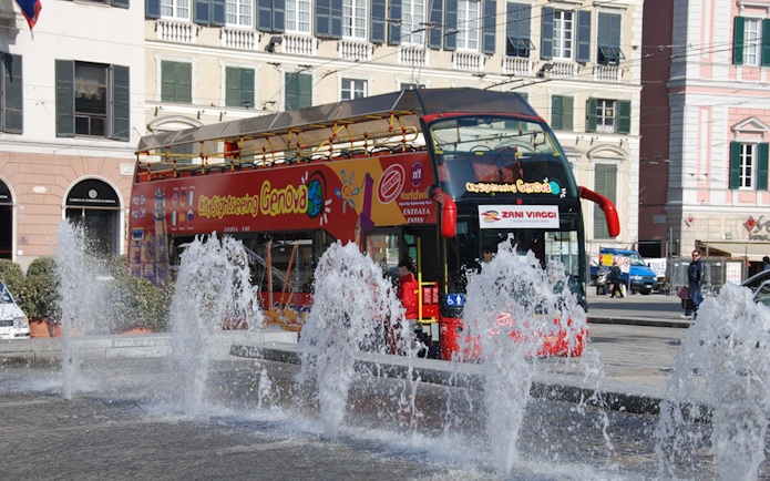 Hop-on-hop-off bus near fountains in Genoa city center.
