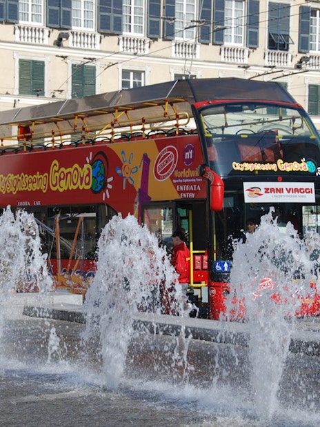 Hop-on-hop-off bus near fountains in Genoa city center.