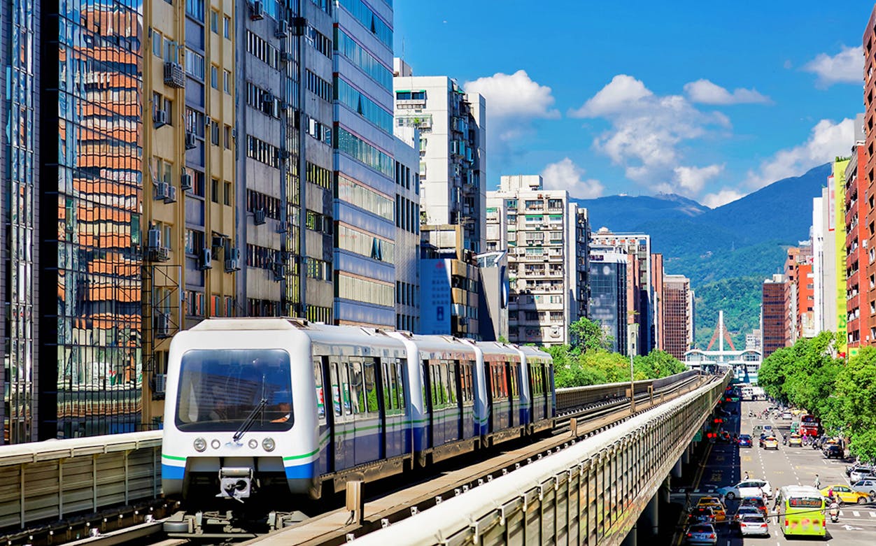 Taipei metro train traveling through cityscape near mountains.