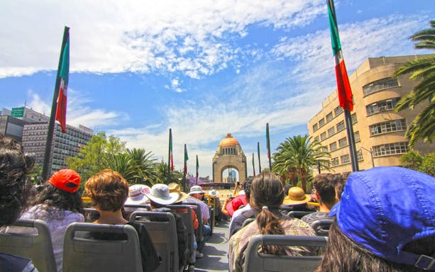Tourists on an open-top bus approaching the Monument to the Revolution in Mexico City.