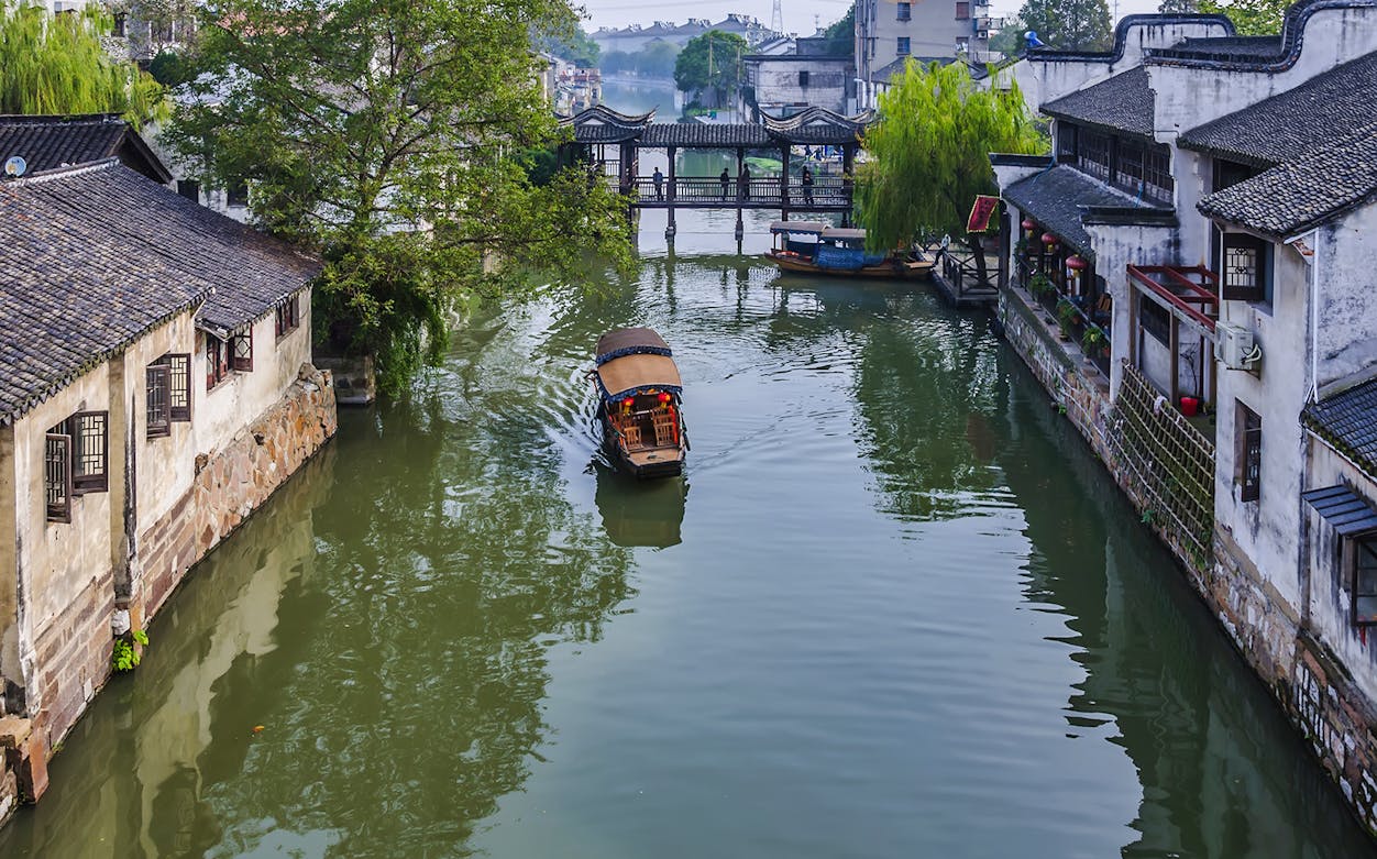 Boat on canal in Zhujiajiao Ancient Water Town, China, with traditional buildings and bridge.