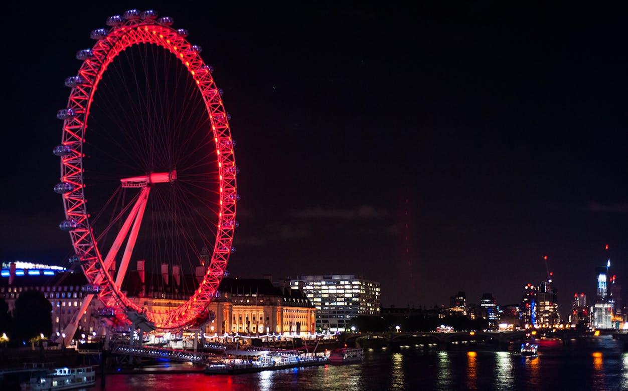 London Eye illuminated at night along the Thames River, London.