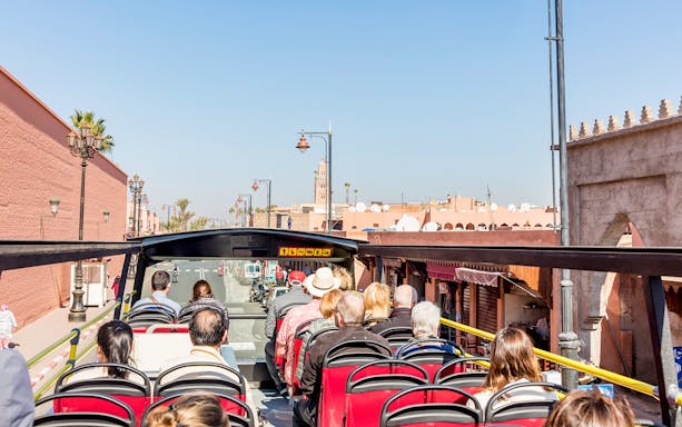 Open-top bus tour in Marrakesh passing city landmarks and palm trees.