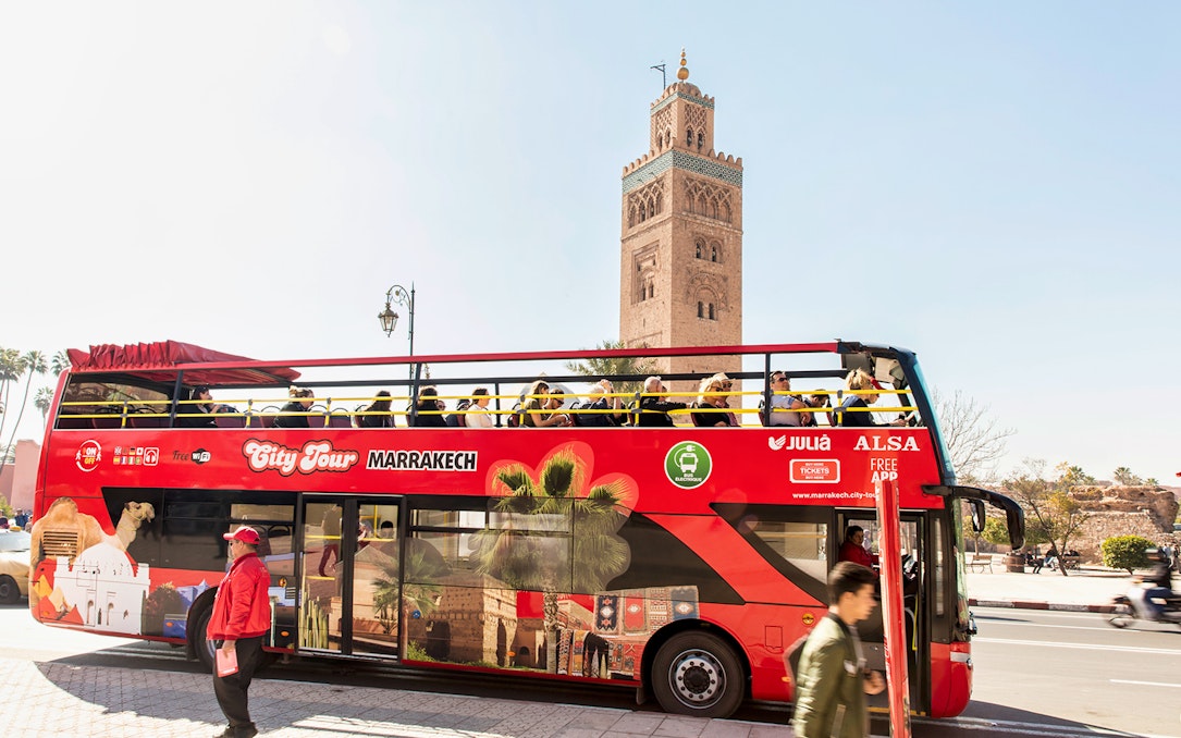 Red double-decker bus on Marrakesh city tour with Koutoubia Mosque in the background.
