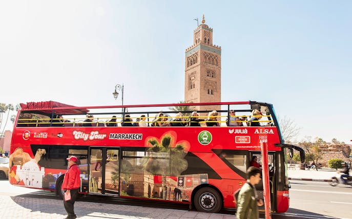 Red double-decker bus on Marrakesh city tour with Koutoubia Mosque in the background.