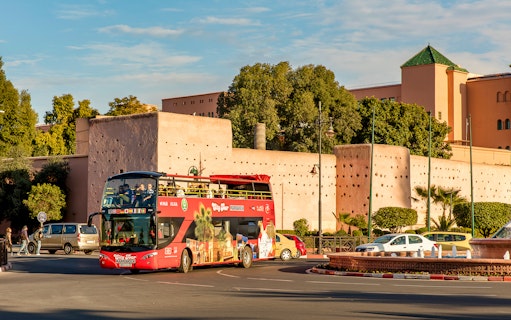 Open-top tour bus in Marrakesh passing historic city walls.