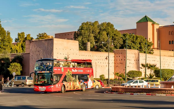 Open-top tour bus in Marrakesh passing historic city walls.