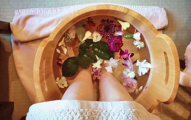 Feet soaking in a wooden tub with flowers during Arashiyu Japanese Foot Massage.