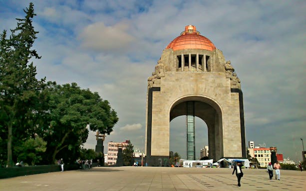 Monument to the Revolution in Mexico City with visitors walking nearby.