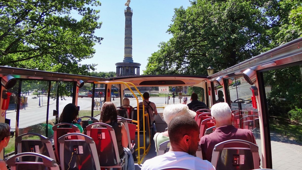 Open-top bus tour with passengers approaching Berlin's Victory Column.