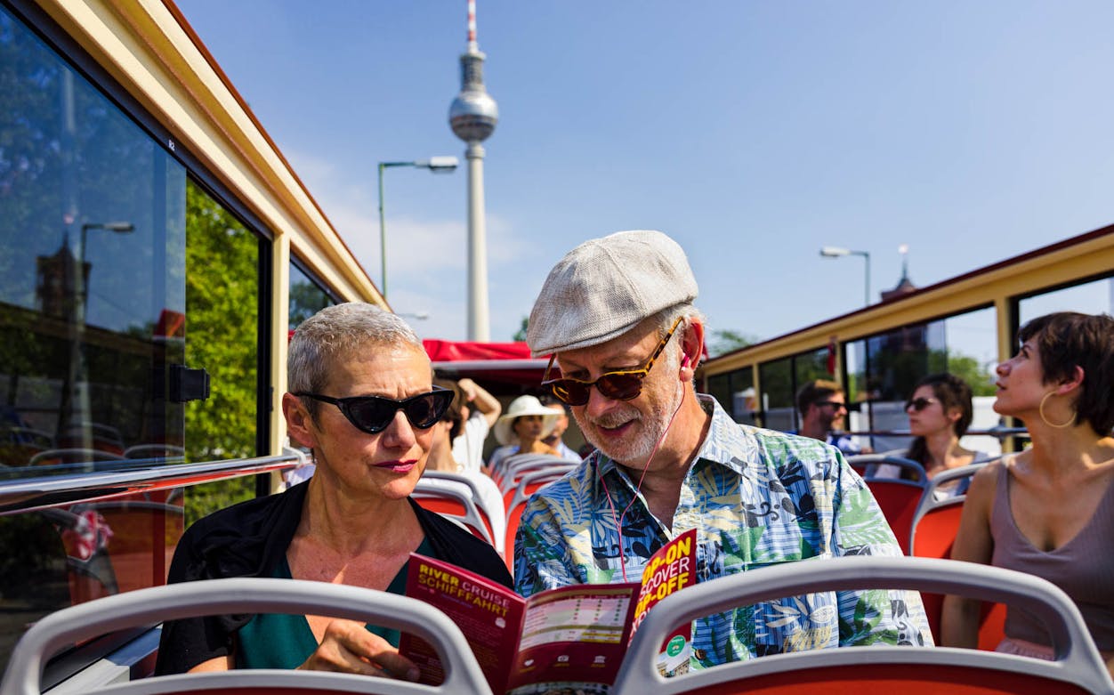Couple on open-top bus tour in Berlin with TV Tower in background.
